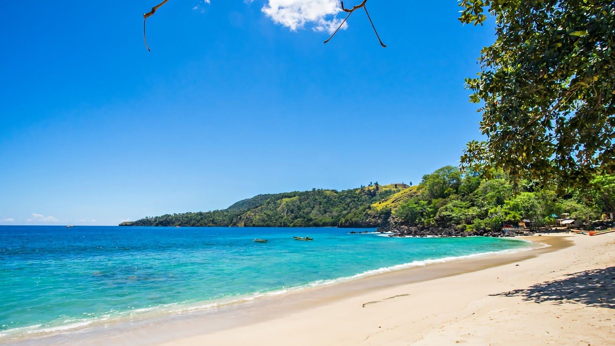 Pantai Pulisan dengan pasir hitam vulkanik yang kontras dengan air laut biru gelap dan langit cerah