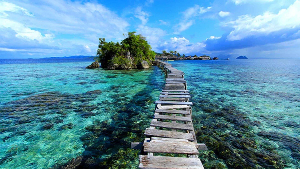 pantai pasir putih Pulau Siladen dengan air laut biru jernih dan perahu kayu di tepi pantai