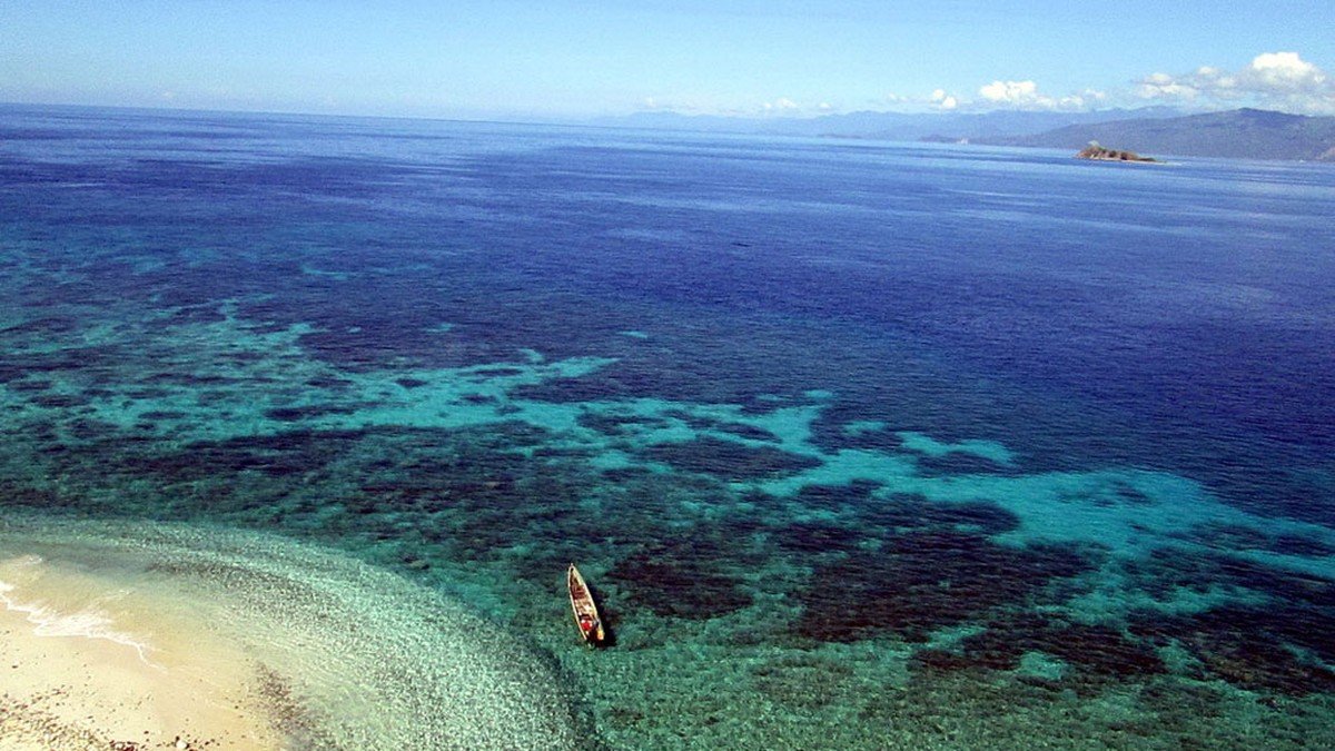 perahu kayu di sekitar Pantai Tumbak dengan pulau-pulau kecil berpasir putih di latar belakang