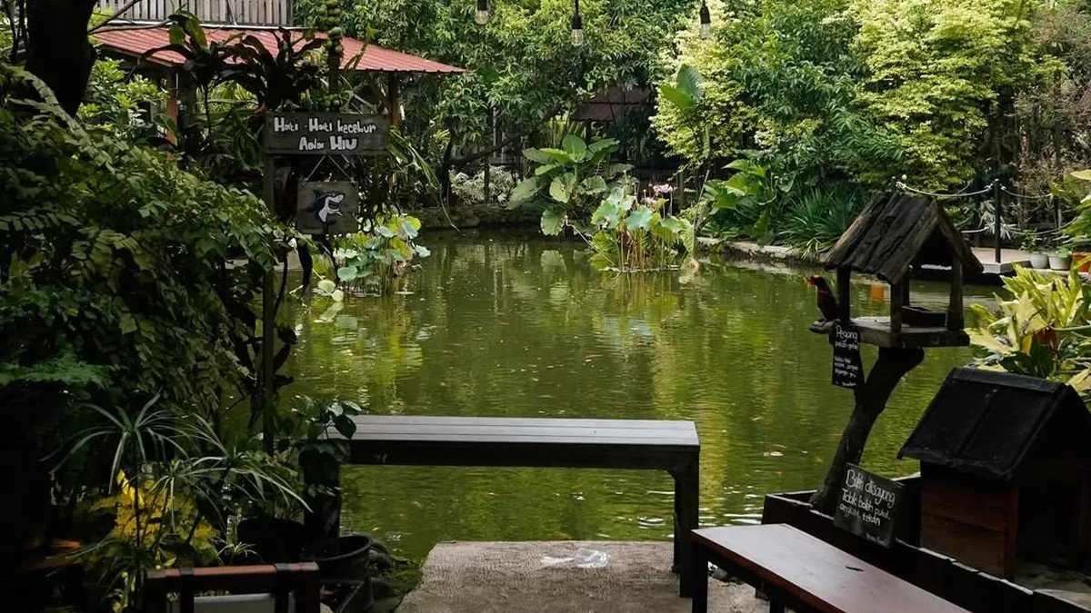 Suasana homey Omah Kopi 78 Depok dengan bangunan kayu, tanaman rindang, dan kolam ikan