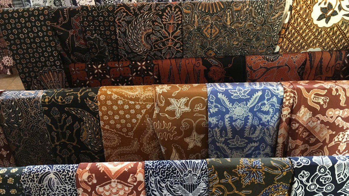 Pembatik sedang mengerjakan batik tulis dengan canting di atas kain mori putih dengan motif parang