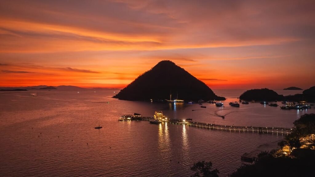 Pemandangan panoramik Pantai Pink Komodo dengan air turquoise dan bukit savana di belakang