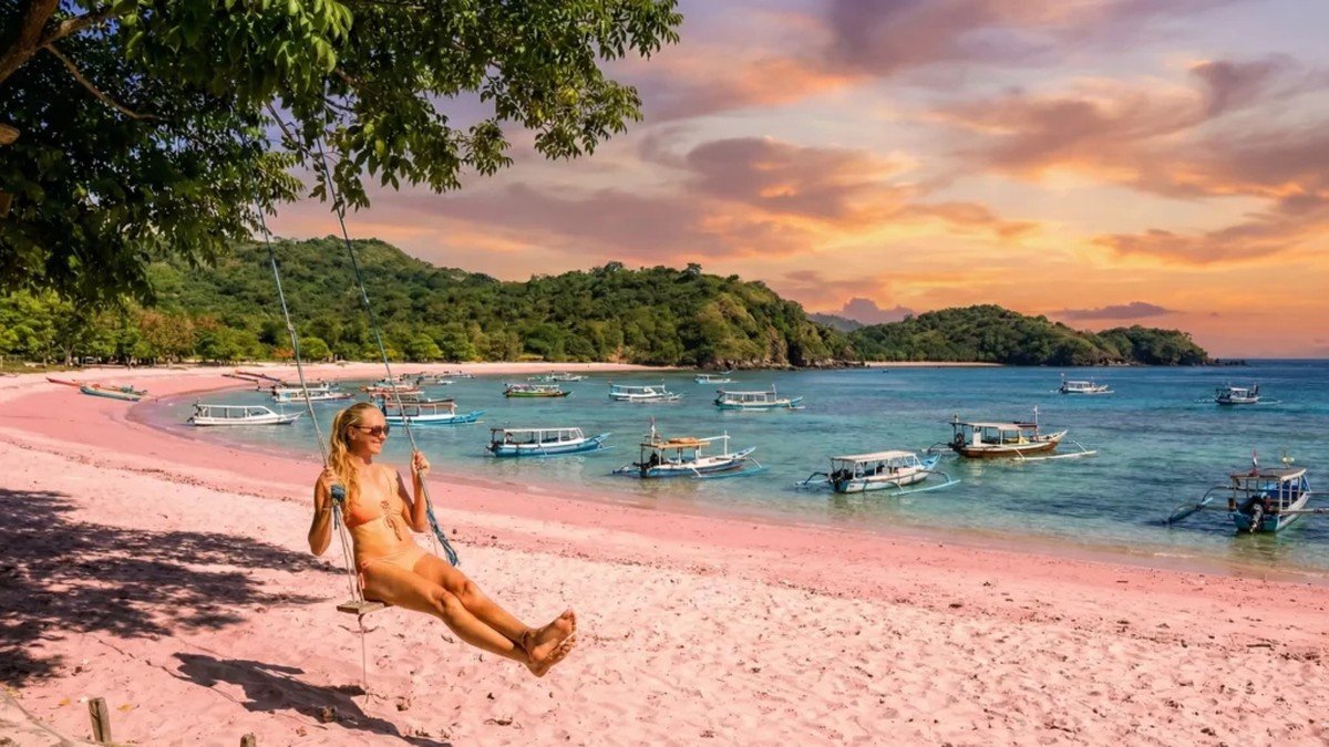 Hamparan pasir berwarna merah muda di Pantai Pink Pulau Komodo dengan latar belakang laut biru jernih dan perbukitan hijau