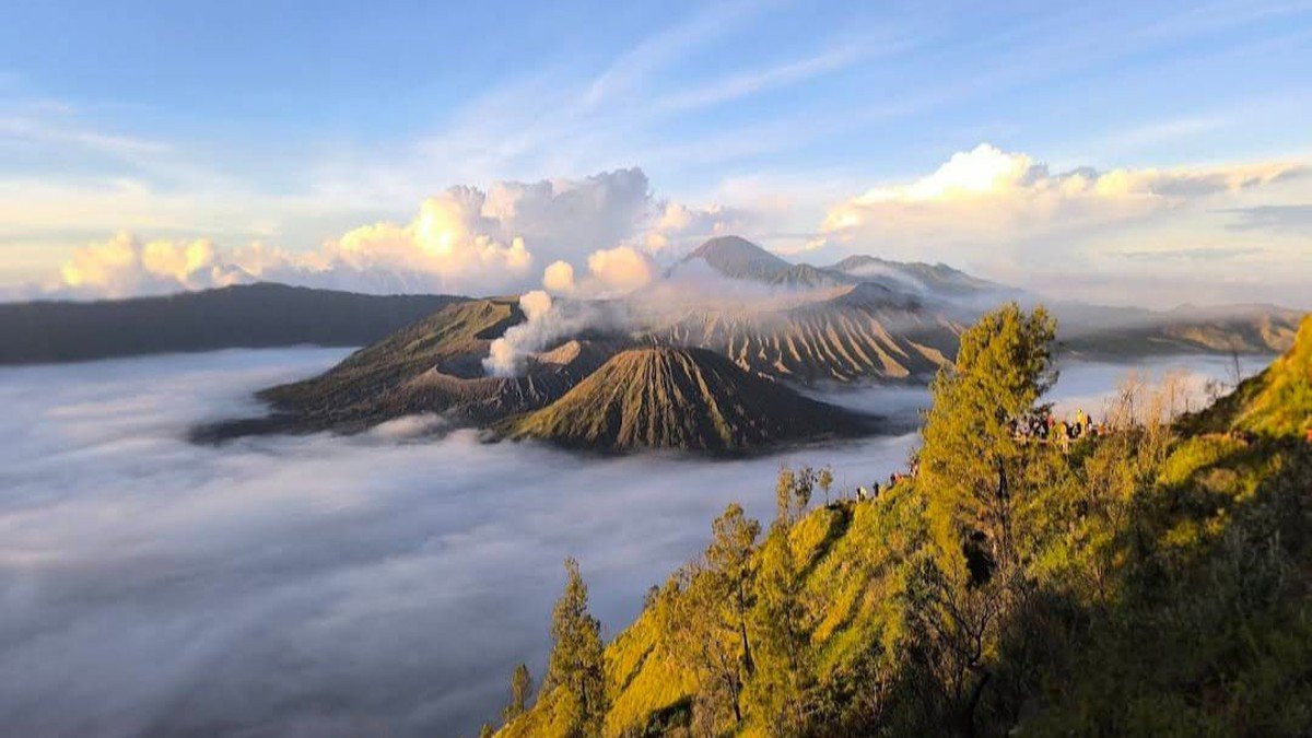 panorama wisata Bromo saat golden hour dengan lautan pasir dan asap kawah di latar belakang
